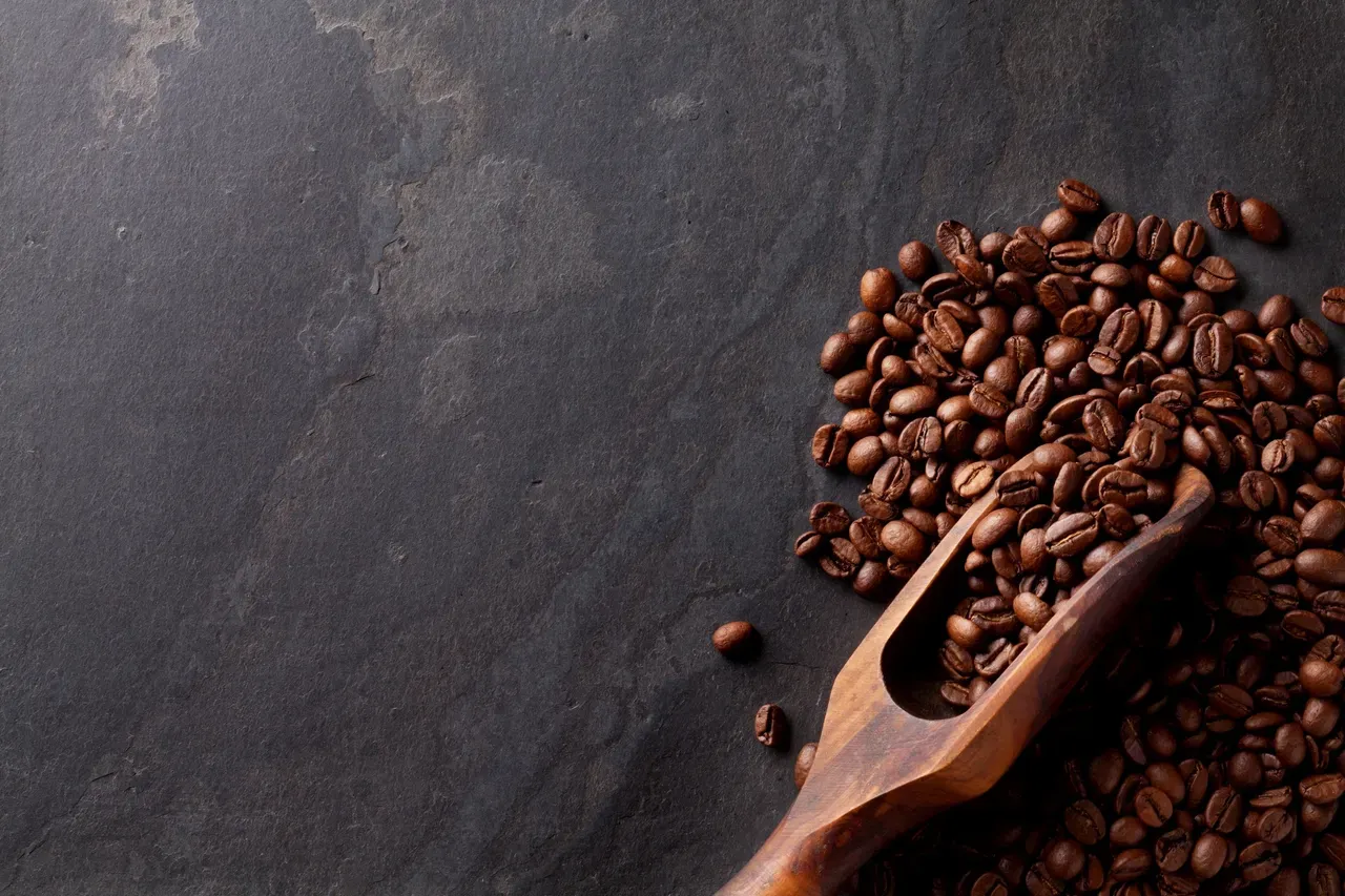 Coffee beans on dark surface with wooden scoop